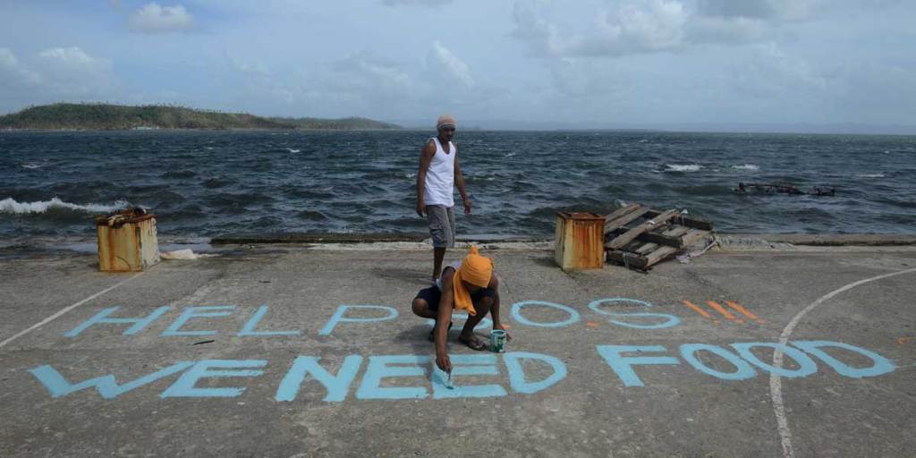 A man in Tacloban paints a message on a baskeball court that reads "Help SOS We Need Food".