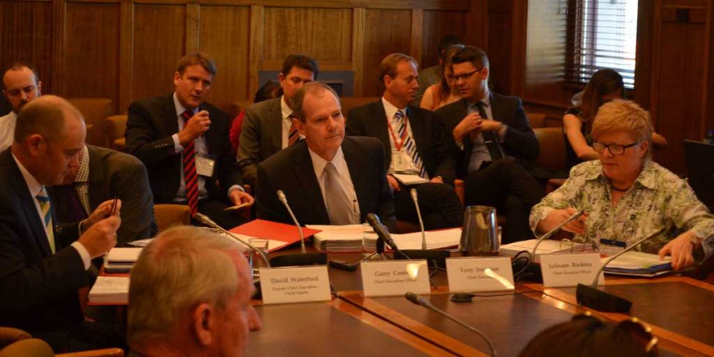 Education department boss Tony Harrison (centre) appearing before Parliament's budget and finance committee today.