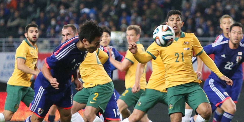Japan midfielder Makoto Hasebe heads the ball while Australia's forward Massimo Luongo (R) attempts to block.