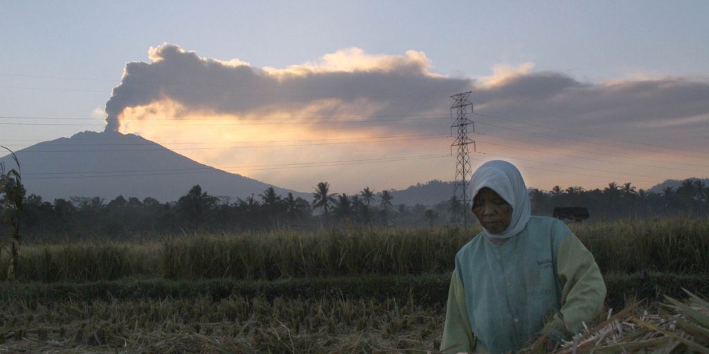 An Indonesian farmer at work while the Mount Raung volcano emits a column of ash and steam.