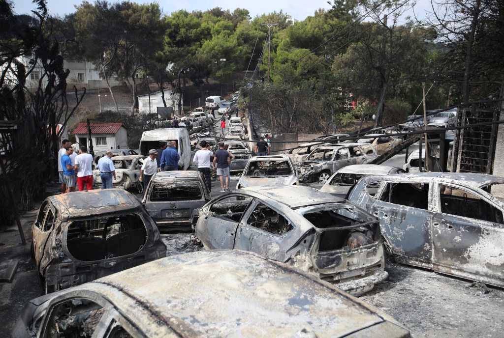 People stand amid the charred remains of burned-out cars in Mati east of Athens. Photo: AP/Thanassis Stavrakis