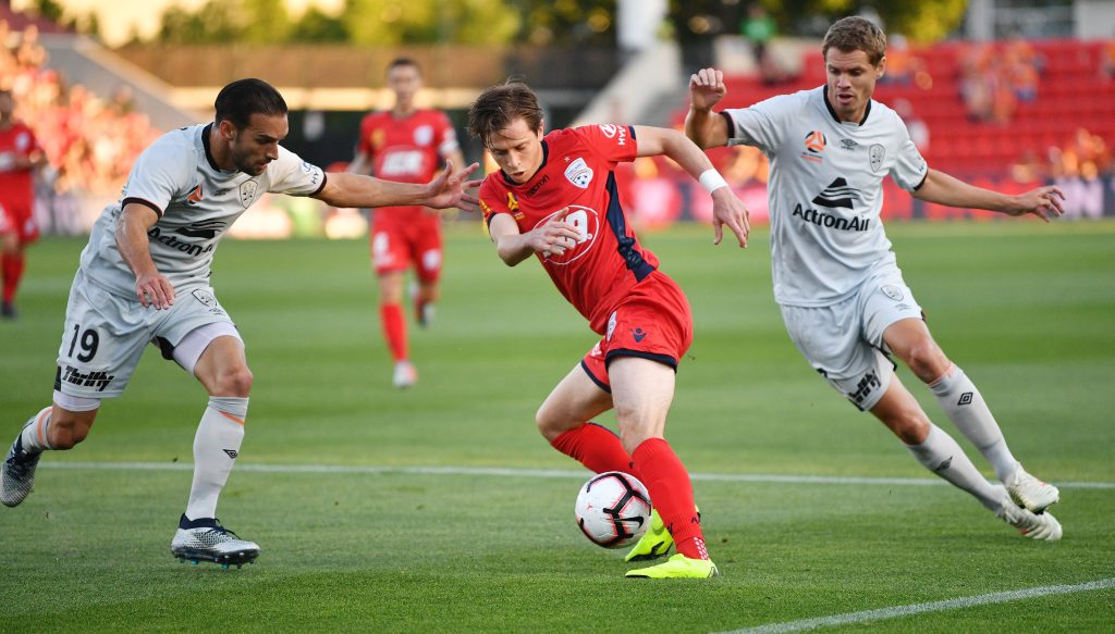 Craig Goodwin of United is tackled by Jack Hingert and Thomas Kristensen of Brisbane Roar on Friday. Photo: AAP/David Mariuz