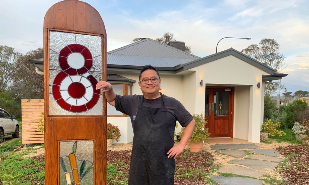 Francis Tan alongside the Lot 8 sign, crafted by an Aldinga Arts EcoVillage resident.