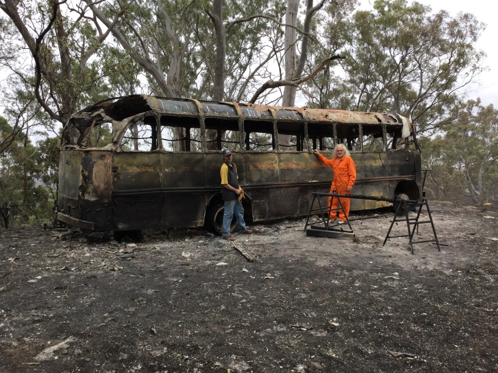 Daniel Kelly (right) and Mathew Fowler next to Kelly's burnt out heritage bus on his property at Lobethal. Photo: AAP/Kathryn Bermingham